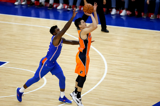 NBA 比赛现场，球员在三分线外起跳投篮，防守球员紧随其后