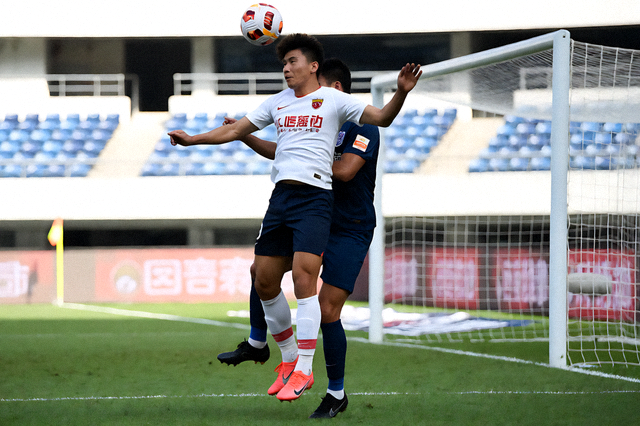 足球联赛夜间比赛现场，球员在禁区内争抢头球